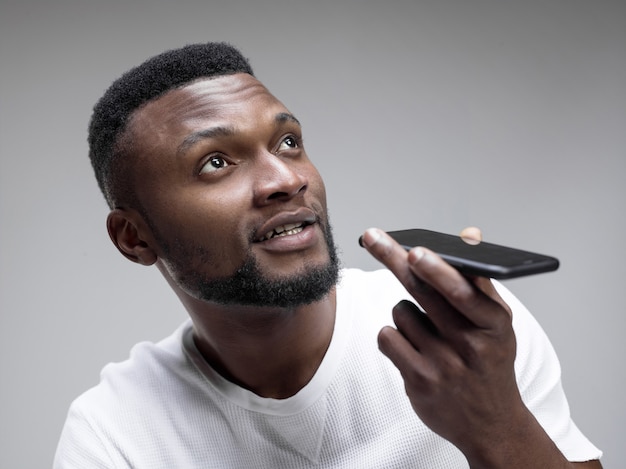 Retrato interior de um homem negro jovem e atraente segurando um smartphone em branco