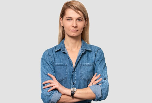 Retrato interior de una mujer independiente caucásica seria de apariencia agradable con cabello rubio vestido con una camisa de mezclilla azul que trabaja distantemente en casa Mujer de negocios posando en la pared blanca del estudio