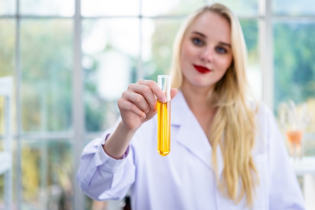 Retrato de una investigadora que lleva a cabo una investigación en un laboratorio de química científico sosteniendo un tubo de ensayo con muestra en el fondo de análisis de laboratorio