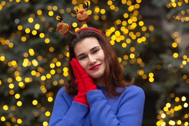 Retrato de invierno de una joven alegre lleva un aro de pelo divertido en el fondo del árbol de año nuevo con luces