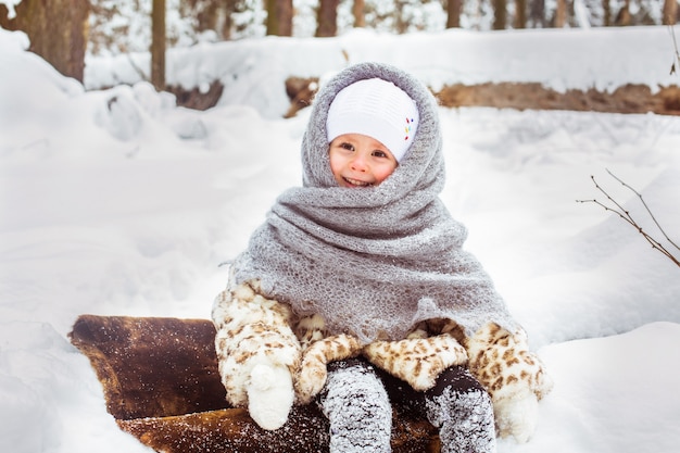 Retrato de invierno de lindo niño sonriente niña en el paseo en el soleado bosque nevado