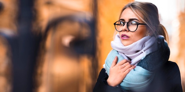 Retrato de invierno de una mujer joven con anteojos que endereza su bufanda