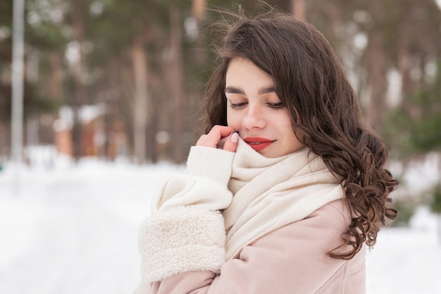 Retrato de invierno de una tierna mujer morena lleva bufanda y abrigo caminando en el bosque. Espacio vacio