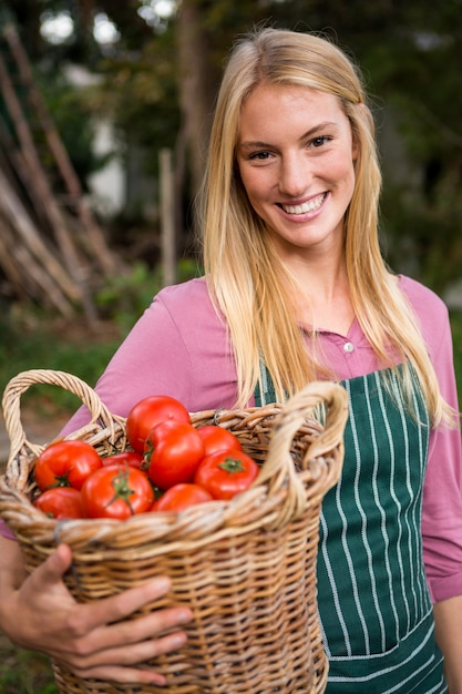 Retrato de jardinero feliz llevando cesta de tomates en el jardín