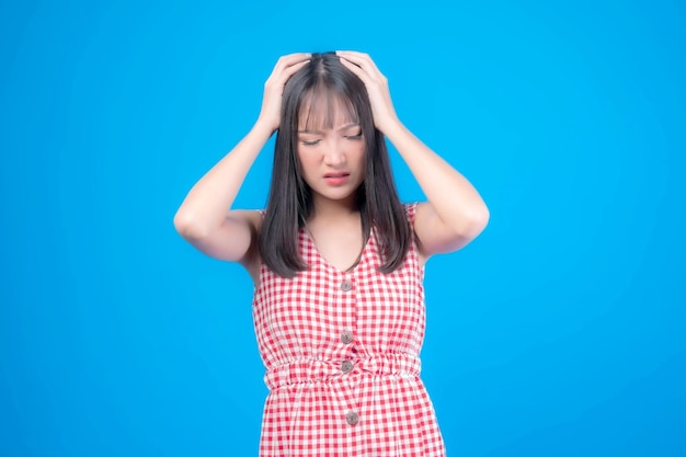 Retrato jovem asiática usou as mãos para cabeça grotescamente em seu cabelo com a mordida dos dentes por causa do espaço de cópia de estresse no fundo azul