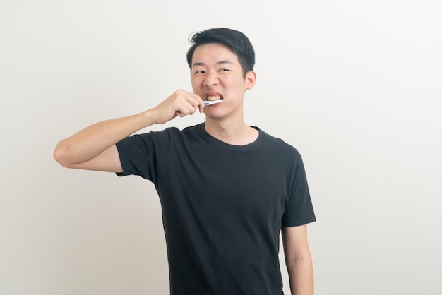 Retrato jovem asiático escova os dentes no fundo branco