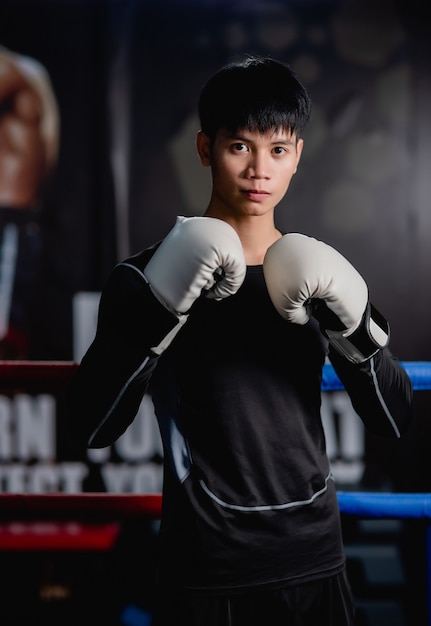 Retrato jovem bonito em roupas esportivas e luvas de boxe brancas em pé pose na tela no ginásio de fitness, aula de boxe de treino de homem saudável,