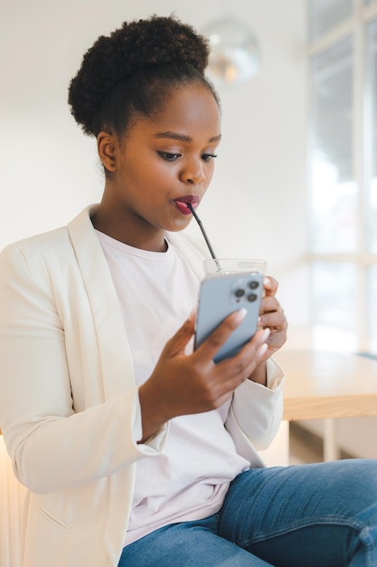 Retrato jovem de etnia africana no café bebendo café gelado no café com o celular nas mãos Conceito de tecnologia de Internet Retrato de negócios Férias de verão Conceito de férias de verão