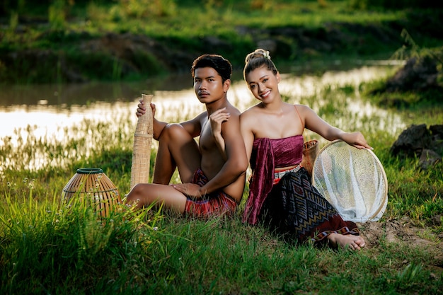 Retrato Jovem de topless vestindo tanga em estilo de vida rural, sentado perto de uma mulher bonita com armadilha de pesca de bambu