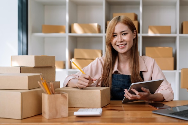 Retrato jovem e atraente empresa de inicialização dona da ásia olhe para o trabalho da câmera feliz com caixa de papelão em casa prepare a entrega no conceito on-line de comércio eletrônico omnicanal de compras da cadeia de suprimentos de sme