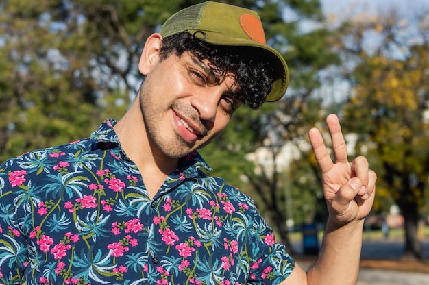 Retrato jovem latino com rolos ao ar livre olhando para a câmera fazendo sinal de v com a mão