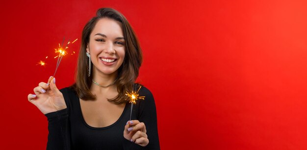 Foto retrato jovem morena feliz em blusa preta segurando com faíscas em fundo vermelho com espaço de cópia