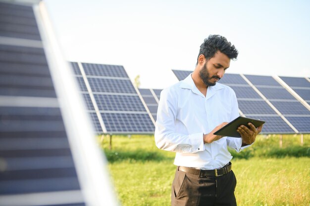 Foto retrato jovem técnico ou gerente indiano vestindo panos formais em pé com painel solar homem de energia renovável em pé com braço cruzado espaço de cópia