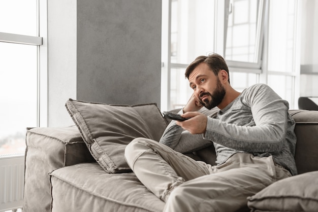 Retrato de un joven aburrido con control remoto de TV