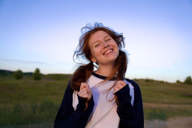 Retrato de una joven adolescente divirtiéndose al aire libre en el campo mirando a la cámara y sonriendo