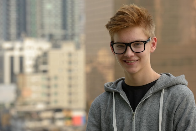 Retrato de joven adolescente guapo contra la vista de la ciudad al aire libre