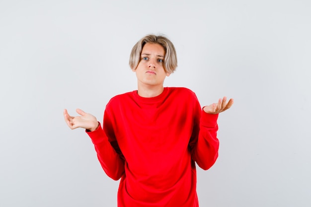 Retrato de joven adolescente mostrando gesto de impotencia en suéter rojo y mirando confundido vista frontal