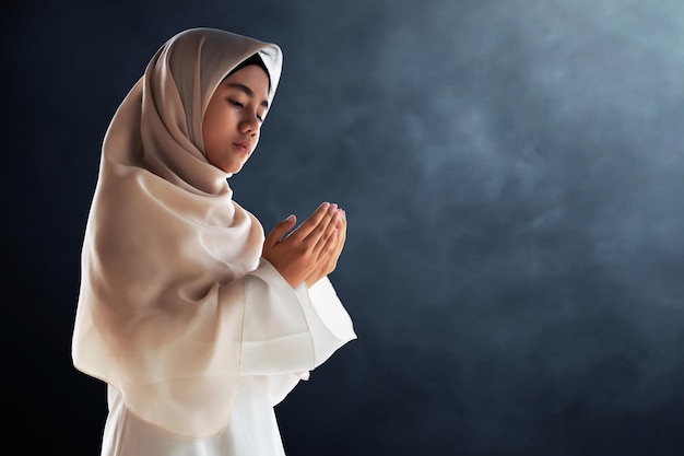 Retrato de una joven adolescente musulmana asiática orando en un fondo oscuro concepto de Eid adha Mubarak