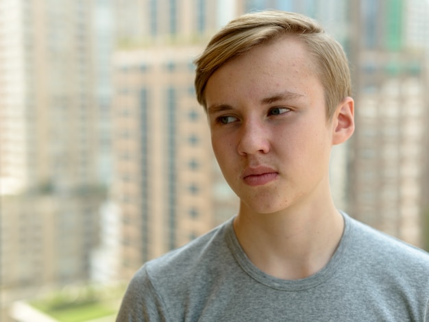 Retrato de joven adolescente rubio guapo contra la vista de la ciudad al aire libre