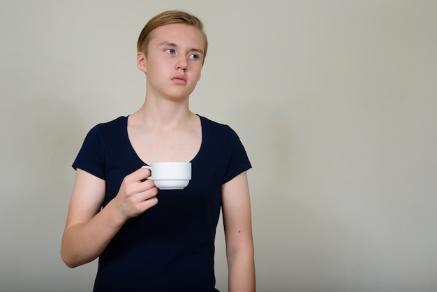 Retrato de joven adolescente rubio guapo pensando mientras sostiene la taza de café