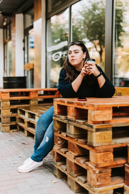 Retrato de una joven adulta con una taza de café cerca de un café en un buen clima otoñal