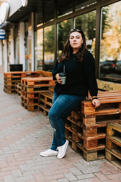 Retrato de una joven adulta con una taza de café cerca de un café en un buen clima otoñal