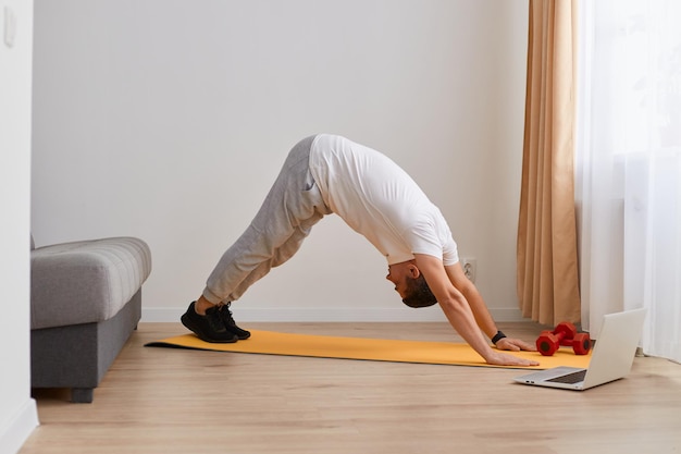 Retrato de un joven adulto caucásico deportivo practicando yoga haciendo ejercicio de perro boca abajo adho mukha svanasana plantean ejercitándose usando ropa deportiva ligera