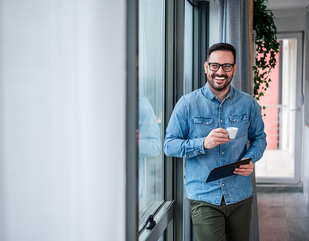 Retrato de un joven adulto sonriente alegre hombre de negocios en la oficina en casa bebiendo café