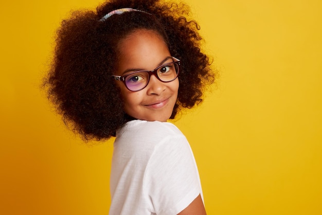 Retrato de una joven africana con anteojos sonriendo y regocijándose en un fondo amarillo limpio