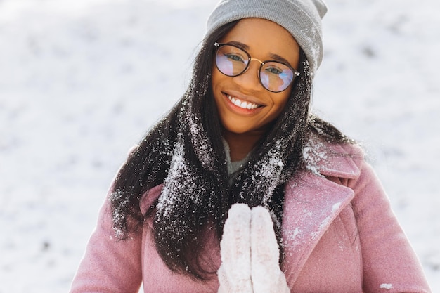 Retrato de una joven africana feliz y positiva con gafas y guantes sonriendo en invierno