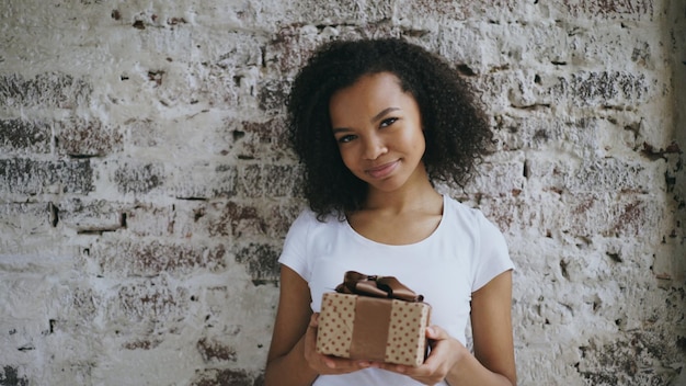 Retrato de una joven africana feliz sosteniendo una caja de regalo y sonriendo a la cámara