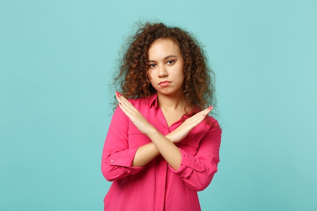 Retrato de joven africana en ropa casual rosa mostrando gesto de parada con las manos cruzadas aisladas sobre fondo de pared azul turquesa. Concepto de estilo de vida de emociones sinceras de personas. Simulacros de espacio de copia.