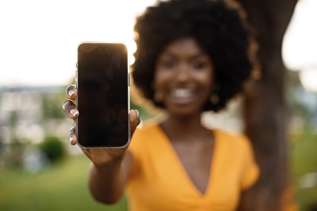 Retrato de una joven africana sonriente sosteniendo un teléfono móvil con pantalla en blanco en la calle