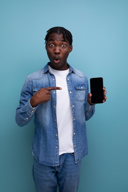 Retrato de un joven africano elegante con rastas en una chaqueta de mezclilla con una maqueta de teléfono inteligente