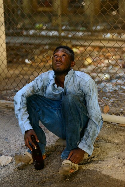 Foto retrato de joven africano sin hogar contra la valla de tela metálica en las calles al aire libre