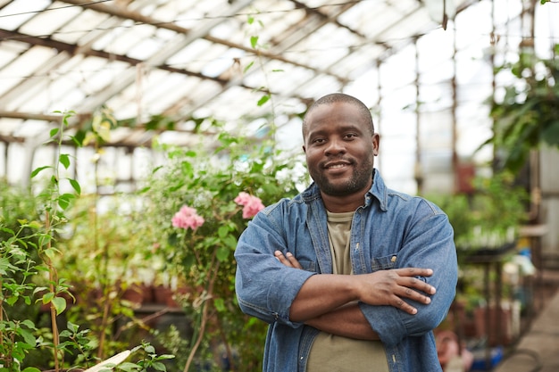 Retrato de joven africano sonriendo a la cámara mientras está de pie en el invernadero