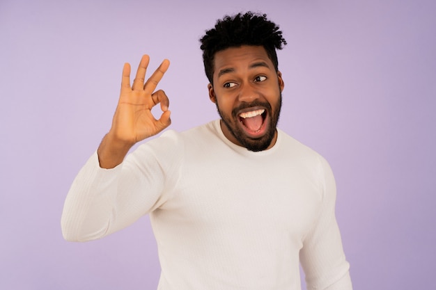 Retrato de un joven afro que hace bien el gesto con las manos y sonriendo mientras está de pie contra el fondo aislado.