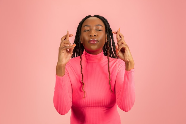 Retrato de joven afroamericana aislada sobre fondo rosa studio, expresión facial.