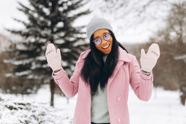 Retrato de una joven afroamericana feliz y positiva con gafas y guantes en el parque de invierno