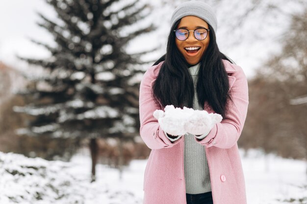 Retrato de una joven afroamericana feliz y positiva con gafas y guantes en el parque de invierno