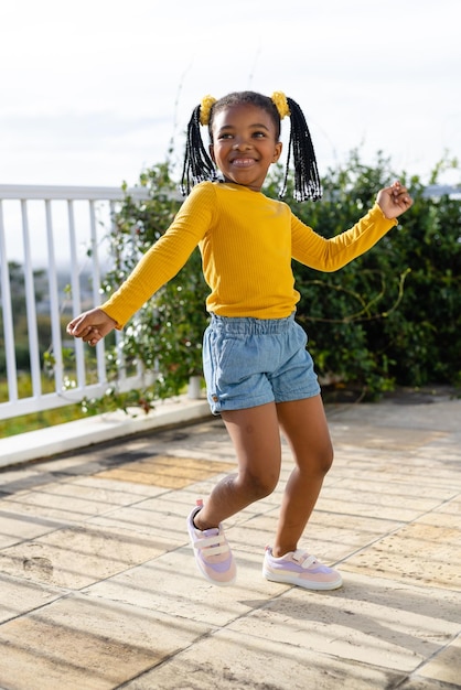 Retrato de una joven afroamericana feliz que se aloja en una terraza soleada. Estilo de vida, naturaleza, infancia y vida doméstica, sin alteraciones.
