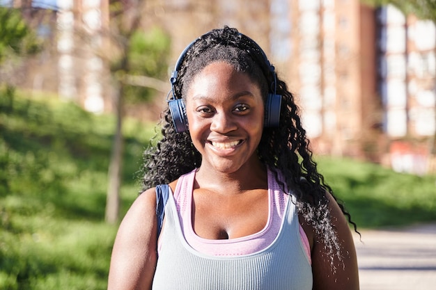 Retrato de una joven afroamericana mirando a la cámara con una sonrisa usando ropa deportiva y auriculares para escuchar música