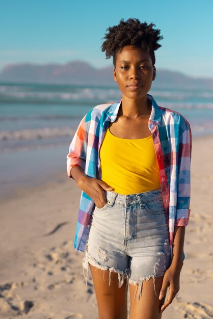 Retrato de una joven afroamericana con el pelo corto y la mano en el bolsillo contra el mar y el cielo azul