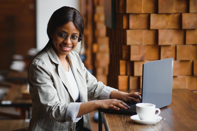 Retrato de una joven afroamericana sonriente sentada en un café con una laptop