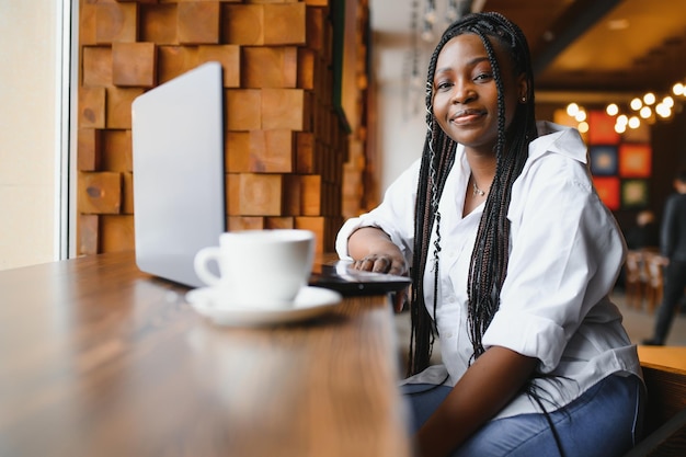 Retrato de una joven afroamericana sonriente sentada en un café con una laptop