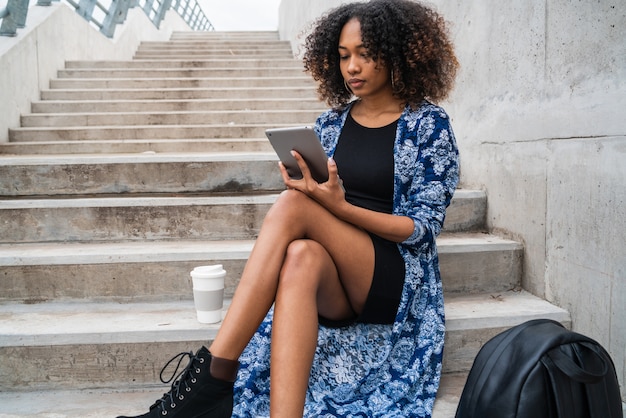 Retrato de joven afroamericana con su tableta digital mientras está sentado en las escaleras al aire libre. Concepto de tecnología.