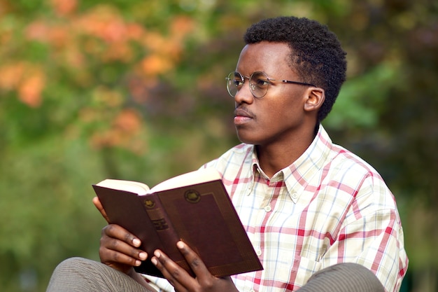 Retrato de un joven afroamericano africano negro inteligente inteligente guapo sentado en un parque y