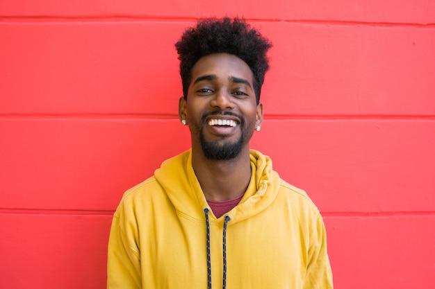 Retrato de joven afroamericano mirando confiado y posando contra la pared roja.