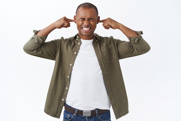 Retrato de joven afroamericano molesto en ropa casual, enfermo y cansado de que el vecino sea demasiado ruidoso