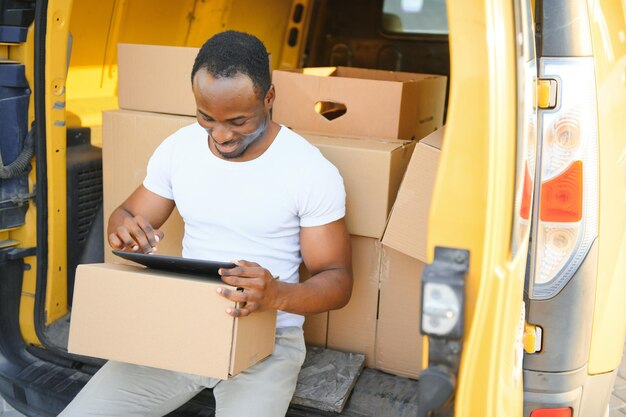 Retrato de un joven afroamericano repartidor de paquetes cerca de un coche con cajas